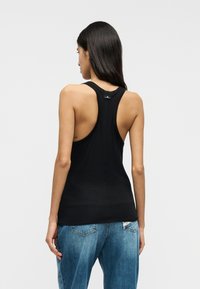 Μαύρο αμάνικο τοπ με σχεδιασμό racerback, κατασκευασμένο από απαλό ύφασμα, εφαρμοστή σιλουέτα και μινιμαλιστική ετικέτα στο πίσω μέρος. Συνδυάζεται με μπλε τζιν παντελόνι.
