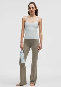 Vaaleansininen toppi ohuilla olkaimilla, yhdistettynä vaaleisiin leveneviin legginsseihin. Malli pitää kädessään vaaleansinistä vesipulloa. Silkkinen kangas näkyy selvästi.