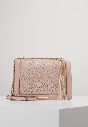 Bolso bandolera rosa claro con diseño intrincado de recortes florales, correa de cadena dorada y charm de borla a juego sobre superficie blanca.