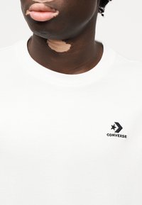 Λευκό κοντομάνικο μπλουζάκι από βαμβάκι, με μαύρο κεντημένο λογότυπο Converse που απεικονίζει αστέρι και βέλος στο στήθος.