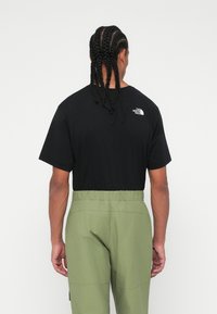 Un tricou negru cu mânecă scurtă, care are un logo alb pe partea superioară a spatelui, asortat cu pantaloni verzi măsliniu cu talie elastică. Material neted, croială lejeră.