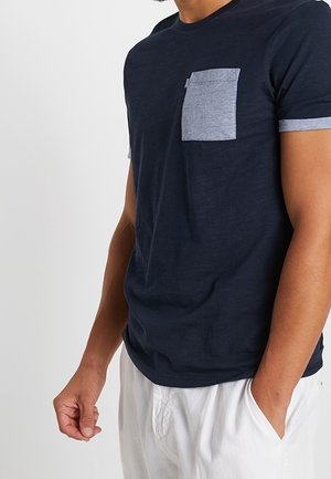 Granatowy t-shirt z krótkim rękawem z szarą kieszenią na piersi i szarymi mankietami, wykonany z miękkiej, teksturowanej tkaniny. Prosty design bez wzorów.