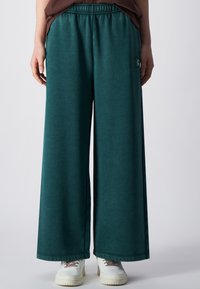 Wijdvallende broek in donkergroene stof, met een elastische tailleband en zijzakken. Gepaarde met witte sneakers, met een ontspannen pasvorm.
