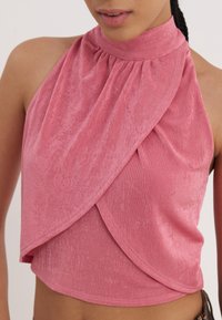 Mouwloze top met halterneck in een gestructureerde lichtroze stof met gedrapeerde voorpanelen en geplooide details bij de hals.