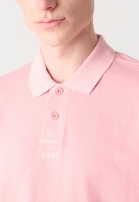 Svetlo roza polo majica iz mehkega blaga, z klasičnim ovratnikom, dvema gumboma in diskretno vezenim logotipom "BOSS".