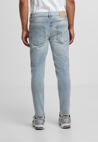 Világos kék farmernadrág, slim fit szabással, öt zsebbel és bézs bőr folttal a deréknál. Texturált anyag enyhe kopással.