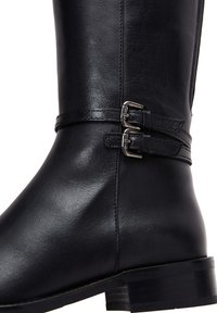 Bota de cuero negra hasta la rodilla con dos hebillas metálicas, una textura suave, punta redonda y tacón apilado.
