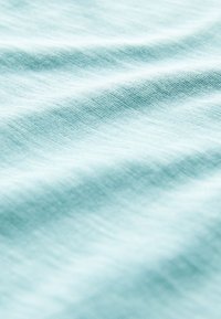 Licht turquoise stof met een zachte textuur, met zachte plooien en een subtiel geweven patroon. Het materiaal oogt glad en licht van gewicht.