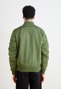 Zaļš bomber stila džemperis ar ribotu apkakli un aprocēm, izgatavots no gludas auduma, ar sānu kabatu un elastīgu vidukļa joslu.