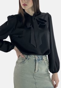 Sort bluse med bindedetalje ved halsen, puffede ærmer, glat tekstur, kombineret med en lyseblå denimnederdel med lommer.