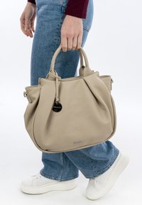 Beige leather handbag with rounded shape, short handles, and silver hardware. Notable textured surface and brand logo detail at the bottom.
