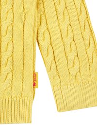Maglione giallo lavorato a maglia con design a trecce e polsini a coste. Comprende un piccolo etichetta rossa con il nome del marchio cucita di lato.