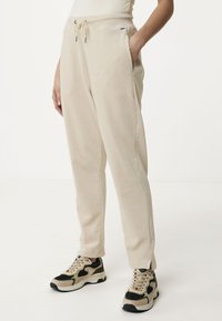 Lichtbeige joggers van zacht materiaal, met een koord in de taille, zijzakken en taps toelopende benen, gecombineerd met zwart en beige sneakers.