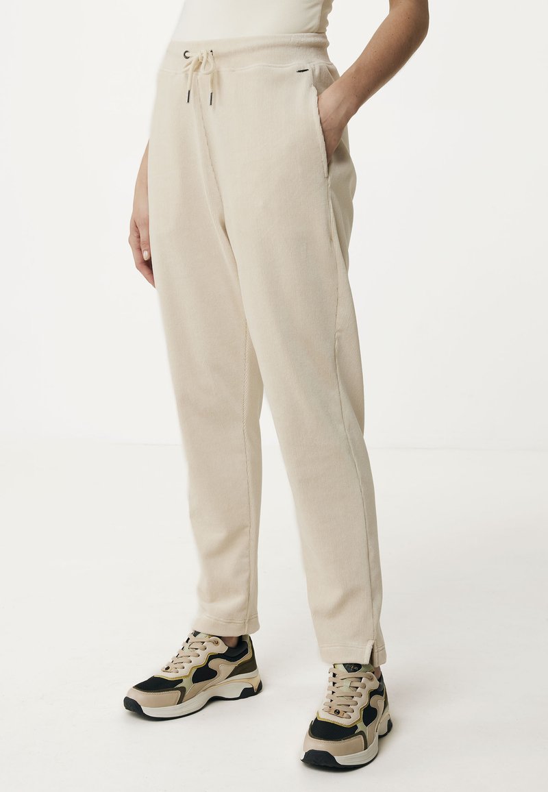 Lichtbeige joggers van zacht materiaal, met een koord in de taille, zijzakken en taps toelopende benen, gecombineerd met zwart en beige sneakers.