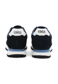 Ein Paar blaue und weiße Turnschuhe, die von hinten gezeigt werden, wobei an jeder Ferse die Zahl "1968" in schwarzem Text zu sehen ist.