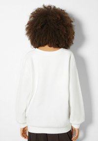 Sweatshirt bianco in pile con una vestibilità ampia, spalle scese e polsini a costine. Texture morbida con un design pulito e minimale.