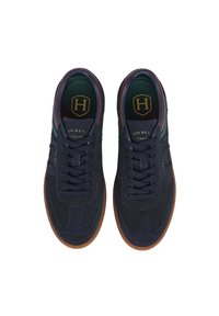 Un par de zapatillas de ante azul marino con suelas marrones, acentos en burdeos y verde, cordones negros y la marca "Hackett London" en las lenguas y los lados.