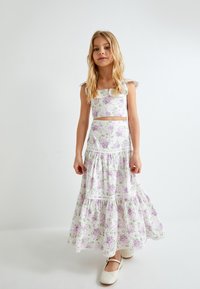 Witte bloemen twee-delige outfit met een crop top met ruches op de schouderbanden en een tiered, enkellange rok, versierd met paarse en groene bloemen.