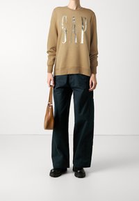 Sudadera marrón con el logo metálico de "GAP", combinada con pantalones cargo holgados en azul marino. Los accesorios incluyen un bolso marrón y zapatos negros gruesos.