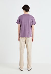 Purple cotton t-shirt with a crew neck, short sleeves, and a relaxed fit, paired with beige straight-leg trousers and white sneakers.