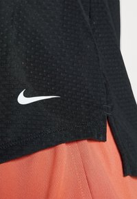 Czarna sportowa koszulka z teksturowanej tkaniny, z białym logo Nike na dolnym lewym brzegu i rozciętym wzorem.