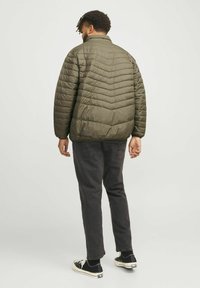 Khaki pufferjack met een chevron-quiltpatroon, hoge kraag en ribgebreide manchetten, gecombineerd met donkere spijkerbroeken en zwarte sneakers. Achteraanzicht.