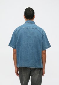 Denimskjorta med kort ärm i ljusblått. Avslappnad passform, knapp-down krage och synliga sömmar. Materialet verkar hållbart med en mjuk textur.