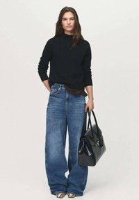 Zwarte trui, losse hooglopende blauwe jeans, gestippelde schoenen en een zwarte handtas. Glad textuur, eenvoudig ontwerp, evenwichtige silhouet.