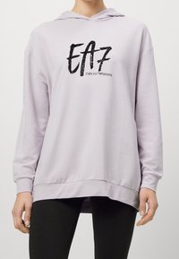 Felpa leggera viola con un fit morbido, maniche lunghe e un logo grafico frontale in nero. Materiale soffice con tasca a marsupio e cappuccio.