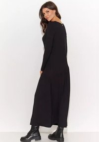 Czarna sukienka z długim rękawem o luźnym kroju, z okrągłym dekoltem i wycięciem na plecach, zestawiona z czarnymi, sznurowanymi botkami.