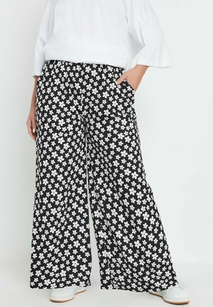Sorte bredbenede bukser med et hvidt blomstermønster, der har lommer og en behagelig taljeelastik. Sammen med hvide sko.