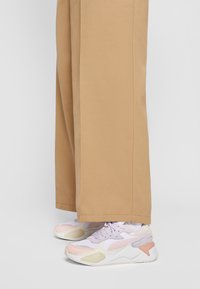 Pantalons légers couleur beige avec une coupe droite, associés à des baskets multicolores avec des panneaux en maille et texturés dans des teintes pastel.