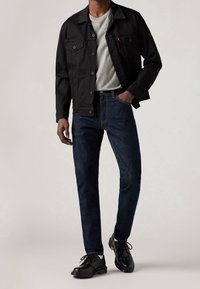 Svart denimjacka med knappstängning, grå t-shirt, mörkblå jeans och svarta skor. Fokusera på enkla, klassiska former och färger.