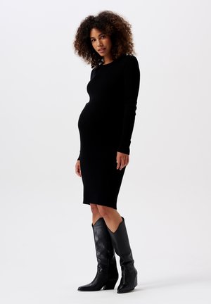 Zwarte gebreide jurk met een aansluitend ontwerp, ronde hals, lange mouwen en midi-lengte. Gecombineerd met zwarte leren laarzen met hoge hakken.