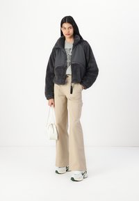Giacca corta grigia e pelosa con un pannello liscio, abbinata a pantaloni beige a gamba larga e sneakers bianche. Insieme a una piccola borsa bianca.