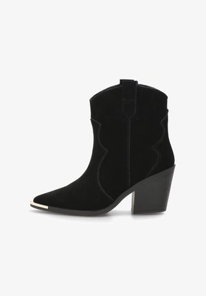 Bota de tobillo de ante negra con puntera puntiaguda, detalles curvados y un tacón grueso. Presenta un pequeño tirador en la parte posterior y un acento metálico en la puntera.