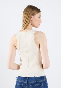 Ribbet beige tank top med bølgete sømmer, en tettsittende design og en rund halslinning, kombinert med blå denimjeans.