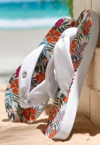 Flip-flops with a white fabric strap, patterned footbed featuring tropical flowers and leaves, and a textured white sole.