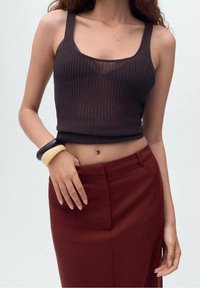 Črn rebrast crop top s kvadratnim izrezom, skladen z visokim bordo krilom. Oblečen z črno-kremnimi zapestnicami na zapestju.