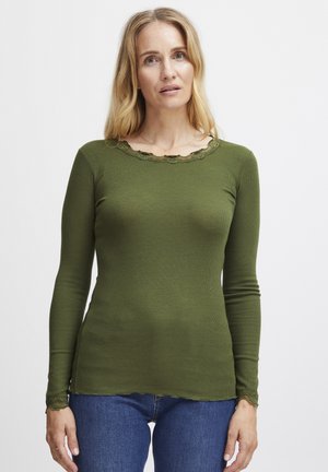 Haut à manches longues de couleur vert olive avec un col et un ourlet en dentelle festonnée, associé à un jean en denim bleu clair.