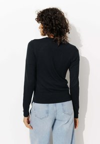 Pull en tricot noir à manches longues, avec des poignets et un ourlet côtelés, design ajusté, porté avec un jean taille haute bleu clair.