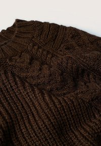 Pull en maille torsadée marron foncé avec poignets et col côtelés, présentant des motifs de couture texturés complexes.