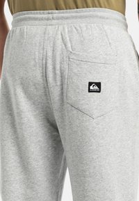 Graue Jogginghosen mit einem elastischen Bund und einer Gesäßtasche, die ein schwarz-weißes Logo zeigt. Weiche Textur mit einem lässigen Design.