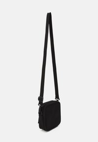 Černá crossbody taška z textilie čtvercového tvaru, s uzávěrem na zip a nastavitelným popruhem. Hladká textura, minimalistický design.