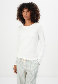 Haut blanc à manches longues avec une finition texturée et un col rond, associé à un pantalon léger à rayures avec des accents bleus subtils.