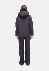 Sort pufferjakke med hætte, der har en glat overflade og quiltet design, parret med løse mørke denimjeans.
