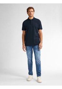 Marineblauwe poloshirt met een kraag en drie knopen, gecombineerd met lichtblauwe jeans en witte sneakers. Eenvoudig ontwerp, gladde textuur.