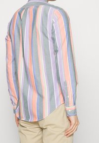 Randig långärmad skjorta med vertikala linjer i pastellnyanser av orange, violett och grå. Knappmanchetter och en rundad fålldesign.