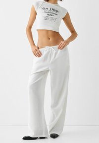 Vita, lätta byxor i linnemix med vida ben och dragsko i midjan. Kombinerat med en kortärmad, vit grafisk t-shirt och svarta ballerinas.