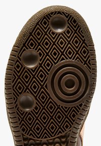 Semelle de chaussure marron avec un motif de semelle en forme de losange, des grips ronds et des bords texturés pour traction et stabilité.